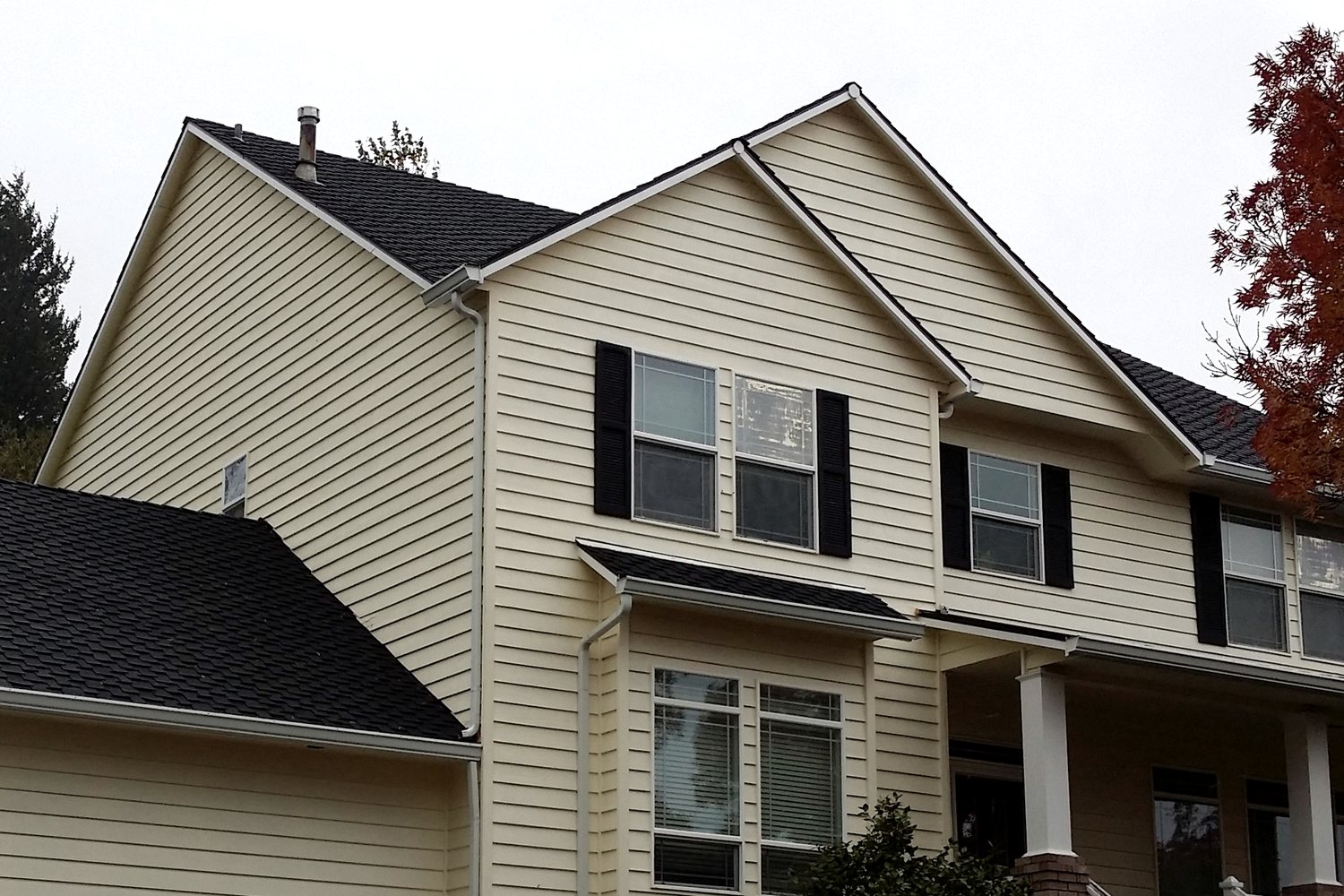 A two-storey house clad in cream lap siding, with one course of siding on the side wall, the rake line of the front gable, the white trim casing down the side of a ground-floor window, and the black shutters flanking an upstairs window all marked — four surfaces an exterior painting bid prices on four different units.