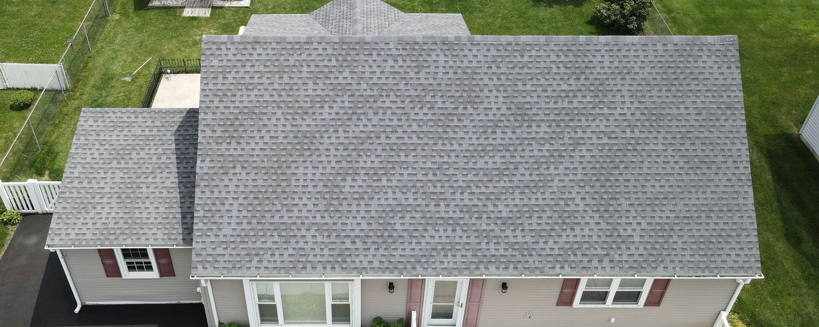 Aerial view of a suburban single-storey house with a newly shingled grey asphalt roof, with its ridge, eave, rake and valley edges marked — the four boundaries a roofer measures when pricing a replacement.
